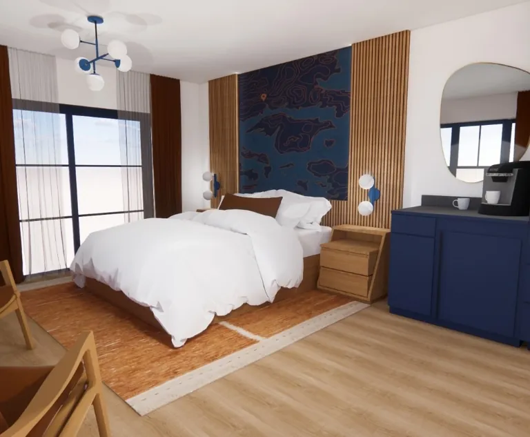 Modern hotel room with a large bed, wooden floors, blue accent wall, navy cabinet, coffee maker, and large window letting in natural light.